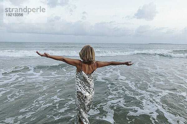 Blonde Frau mit ausgestreckten Armen am Strand