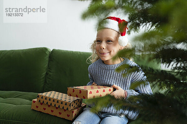 Glückliches Mädchen mit Weihnachtsgeschenken  das zu Hause auf dem Sofa sitzt