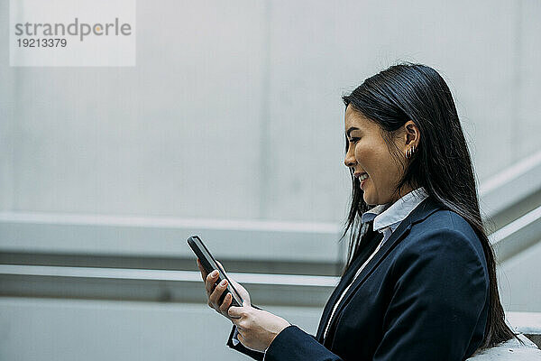 Lächelnde Geschäftsfrau benutzt Smartphone am Arbeitsplatz