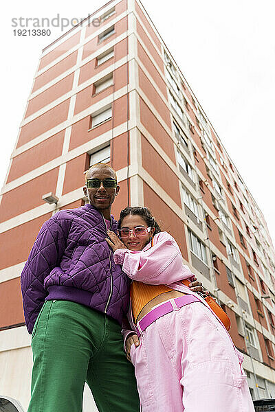 Lächelnde Frau steht mit nicht-binärer Person vor einem Gebäude