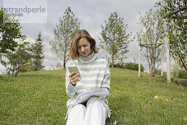 Frau sitzt auf Gras und benutzt Smartphone im Park