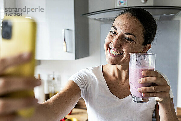 Glückliche Frau klickt zu Hause auf Selfie mit Milchshake