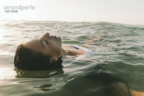 Woman with eyes closed swimming in water at beach