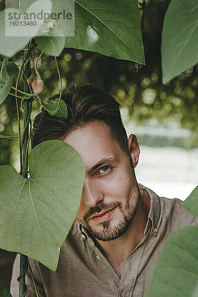 Young man covering eye with leaf in garden