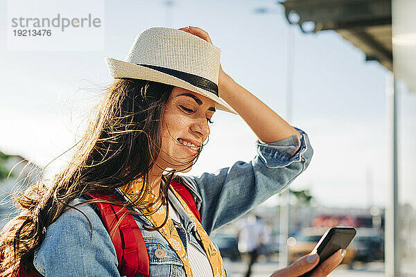 Glückliche junge Frau mit Hut  die ihr Mobiltelefon benutzt