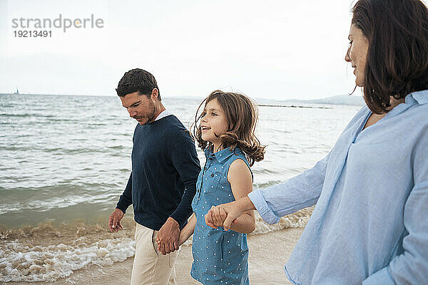 Glücklicher Vater und Mutter halten Händchen mit ihrer Tochter am Strand