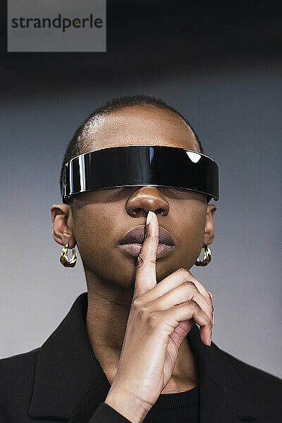 Young woman with finger on lips and wearing smart glasses