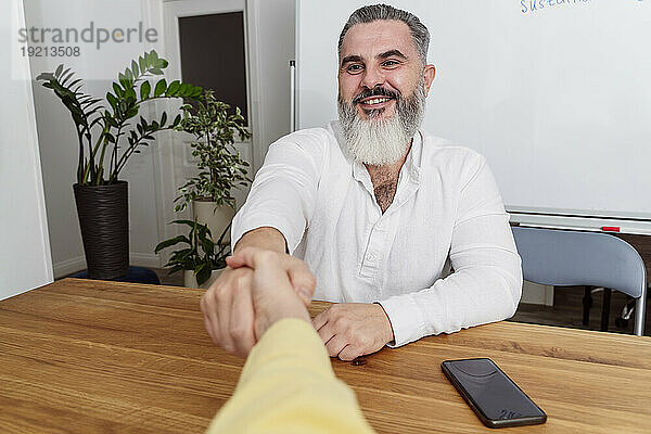 Smiling businessman shaking hand with businesswoman at work place