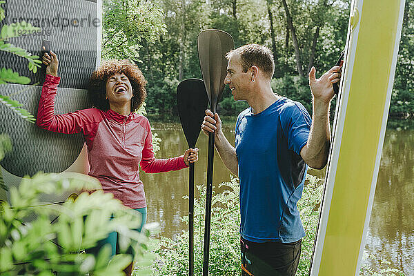 Fröhliche Freunde halten Paddleboards in der Hand und verbringen ihre Freizeit am See