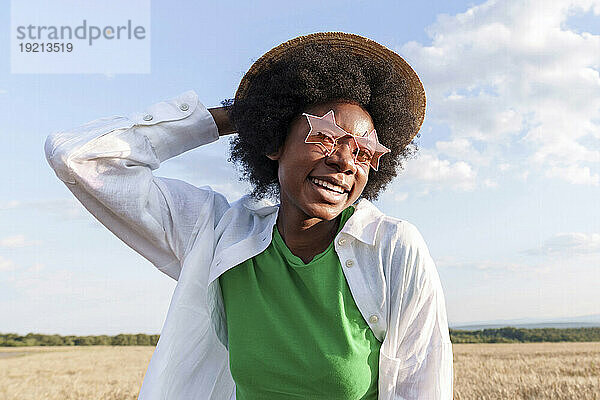Happy afro woman wearing hat and star shape sunglasses in field