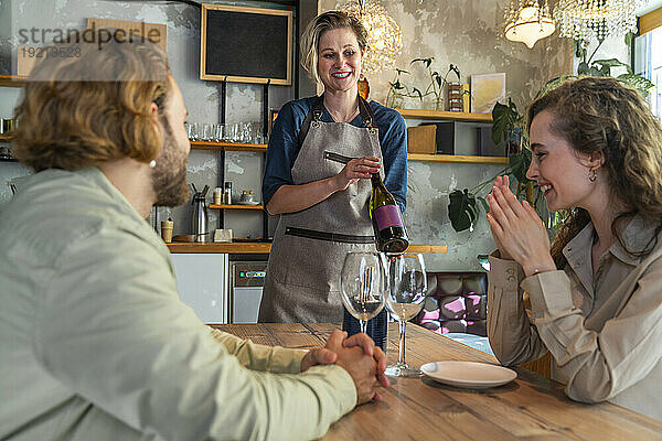 Kellnerin zeigt zufriedenen Kunden im Restaurant eine Weinflasche