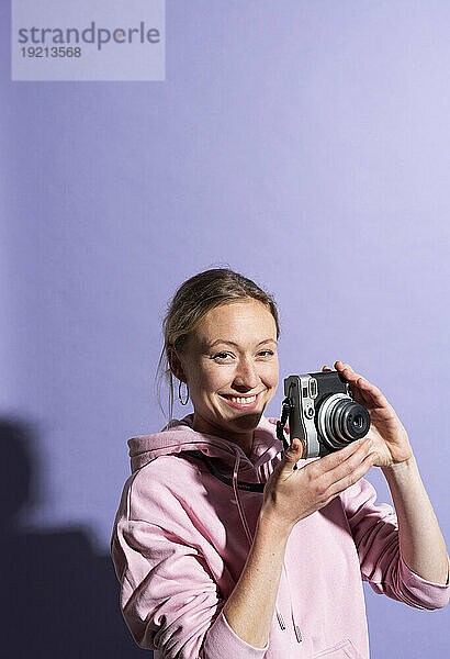 Lächelnde Frau hält Kamera vor violettem Hintergrund
