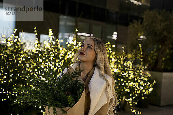 Lächelnde Frau hält einen Blumenstrauß in der Nähe der Weihnachtsbeleuchtung