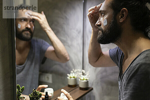 Man applying moisturizer on face in front of mirror