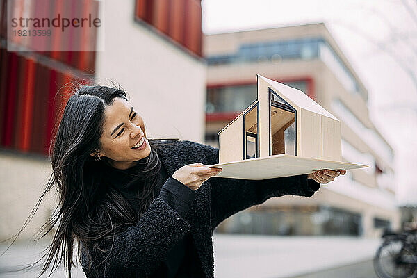 Glücklicher Architekt untersucht Hausmodell vor Bürogebäude