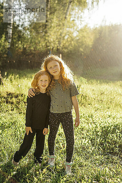 Smiling sisters standing in park on sunny day