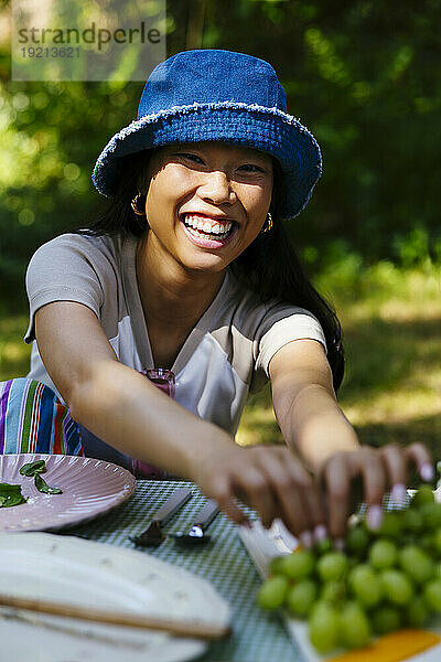 Lächelnde Frau pflückt am Picknicktisch Weintrauben aus der Traube