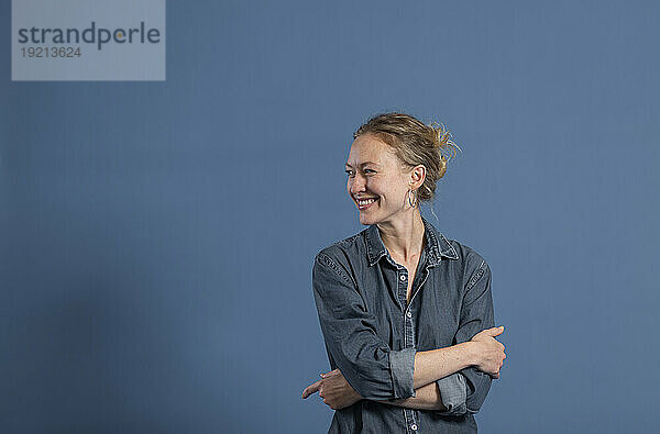 Happy woman with arms crossed against blue background