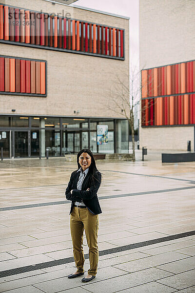 Smiling businesswoman standing with arms crossed in front of office building