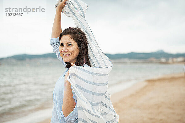 Lächelnde Frau mit Schal  die Spaß am Strand hat
