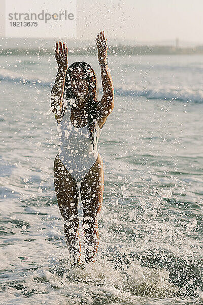 Verspielte Frau steht am Strand und planscht Wasser im Meer