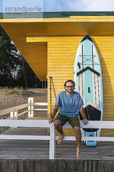 Junger Mann mit Paddleboard in der Nähe der Strandhütte