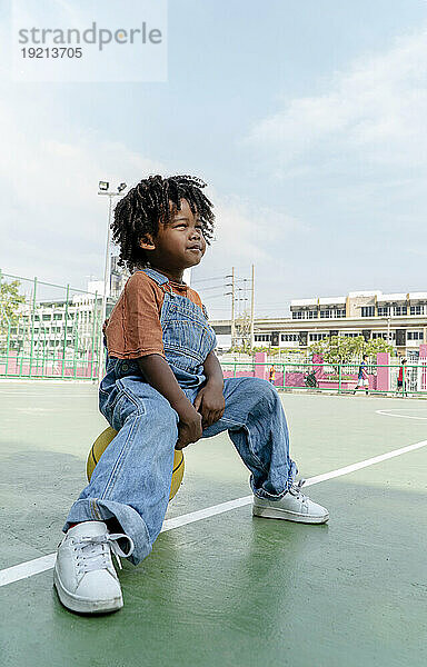 Netter Junge sitzt auf Basketball auf dem Sportplatz