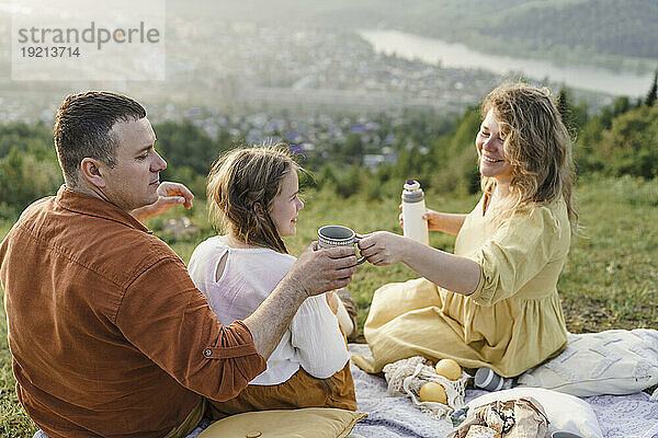 Glückliche Frau serviert einem Mann  der mit ihrer Tochter sitzt  Tee