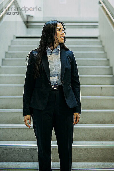 Lächelnde Geschäftsfrau  die auf der Treppe im Büro steht und wegschaut