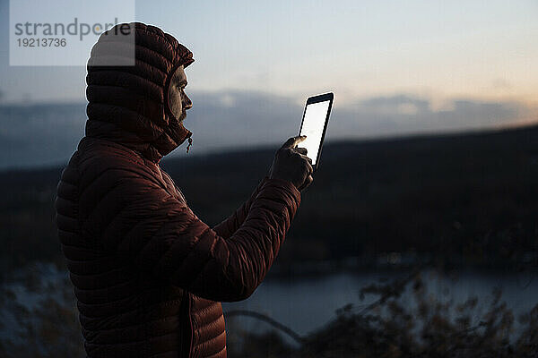 Reifer Mann benutzt Tablet-PC in der Abenddämmerung