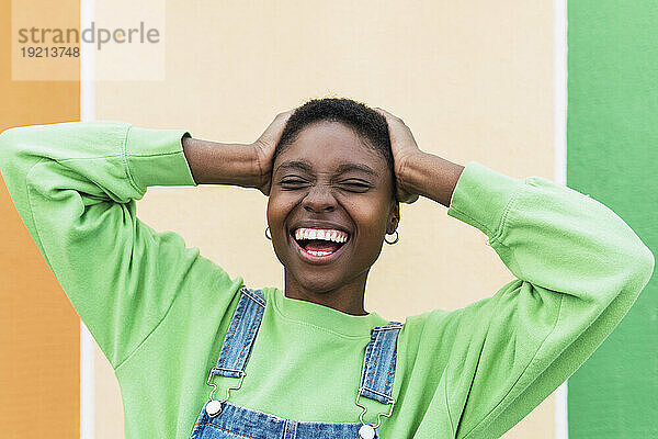 Cheerful woman laughing with head in hands in front of multi colored wall