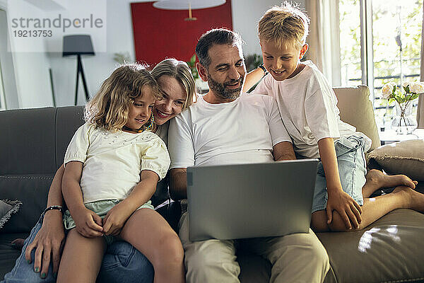 Vater teilt Laptop mit Familie  die im Wohnzimmer sitzt