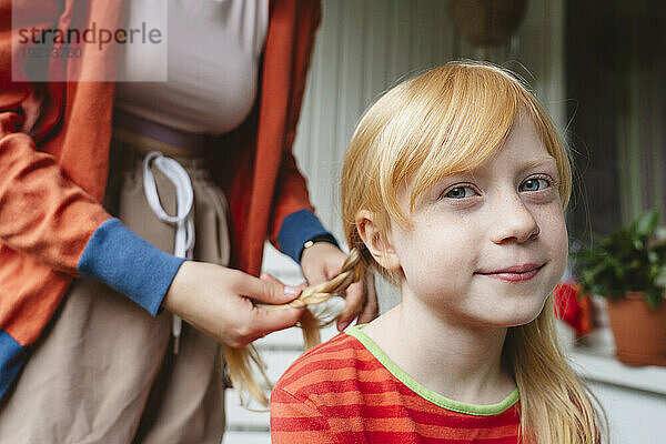 Teenage girl tying braid of blond sister at home