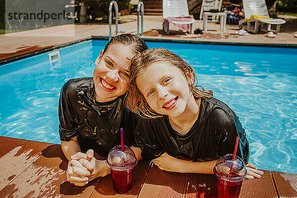 Lächelnde Freunde mit alkoholfreien Getränken am Pool an einem sonnigen Tag
