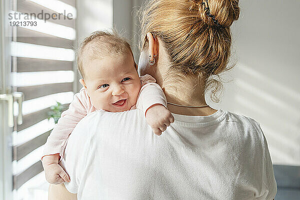 Smiling newborn baby resting on mother's shoulder at home