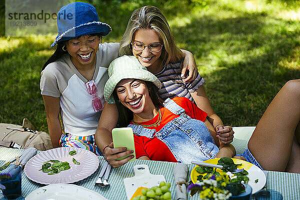 Smiling friends taking selfie at picnic table in garden