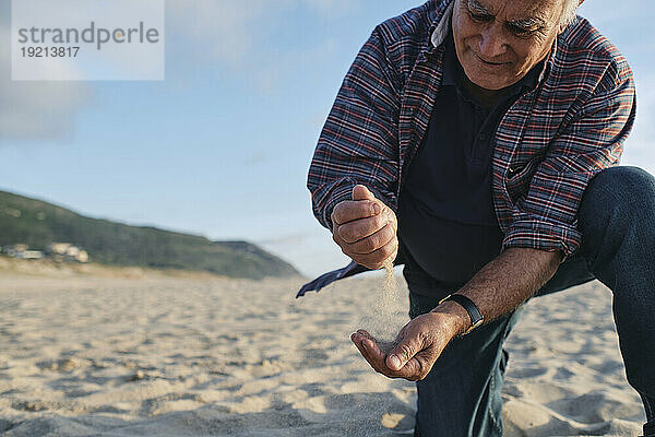 Lächelnder älterer Mann  der am Strand mit Sand spielt