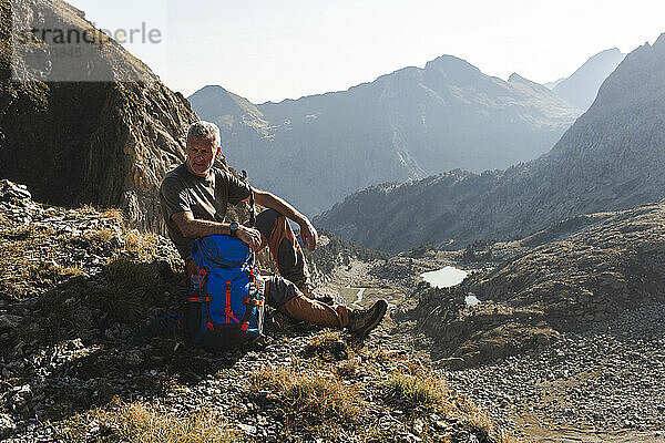 Reifer Mann sitzt mit Rucksack vor Bergen