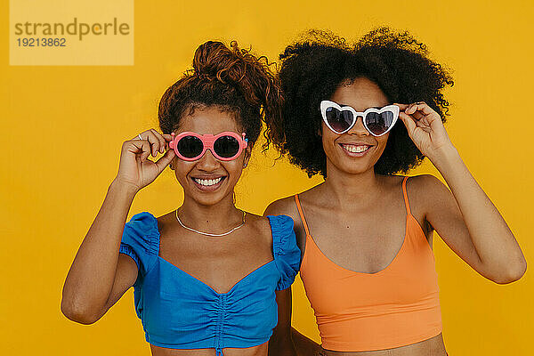 Glückliche Frauen mit Sonnenbrille vor gelbem Hintergrund