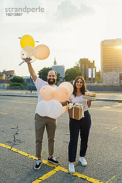 Glückliches Paar hält Luftballons und Geschenke auf der Straße