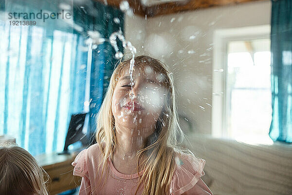 Blondes Mädchen lacht und spuckt zu Hause Wasser aus dem Mund