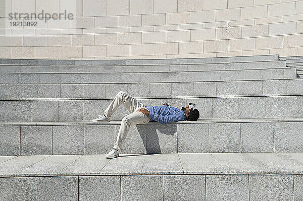 Carefree man wearing virtual reality simulator and lying down on steps