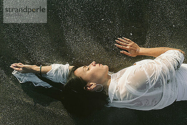 Woman with eyes closed lying on black sand