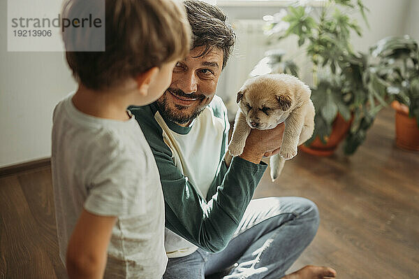 Smiling man showing cute puppy to son at home