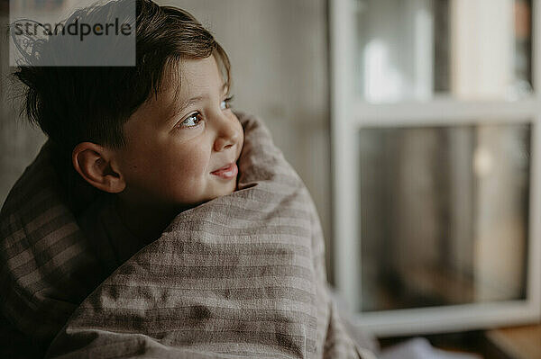 Contemplative boy wrapped in blanket at home