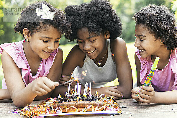 Happy girls with sister lighting birthday candles in garden