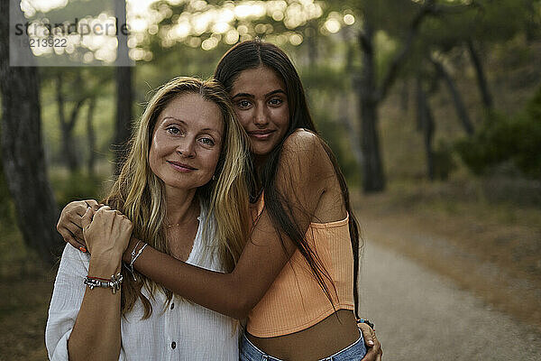 Lächelndes Teenager-Mädchen umarmt Mutter im Wald