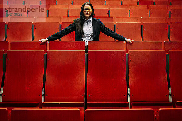 Selbstbewusste Geschäftsfrau inmitten roter Sitze im Kongresszentrum