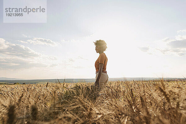 Young woman enjoying solitude in barley field at sunset