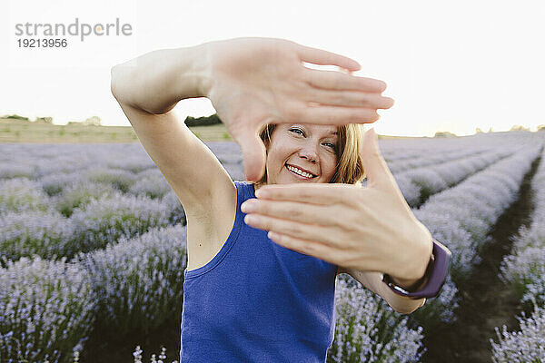 Lächelnde Frau zeigt Fingerrahmenschild im Lavendelfeld